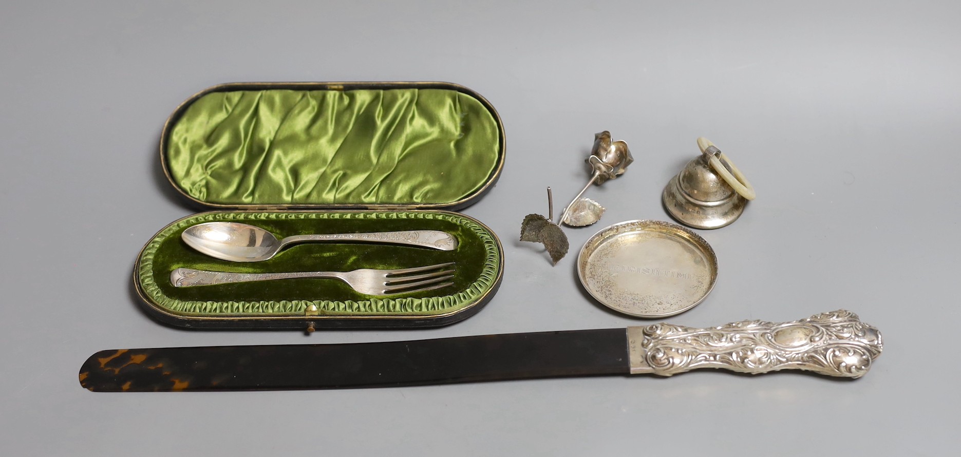 A late Victorian repousse silver mounted tortoiseshell page turner (chip), 39.6cm, a silver rattle, a silver the Irish Times pin tray, 800 standard model of a rose and a cased silver christening pair.